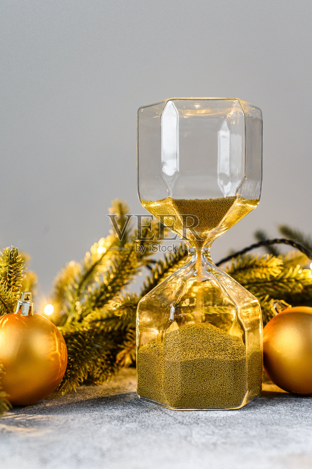 圣诞背景,沙漏用金色的沙子,冷杉树枝和圣诞玩具。即将到来的假期的概念。新年快乐。照片摄影图片