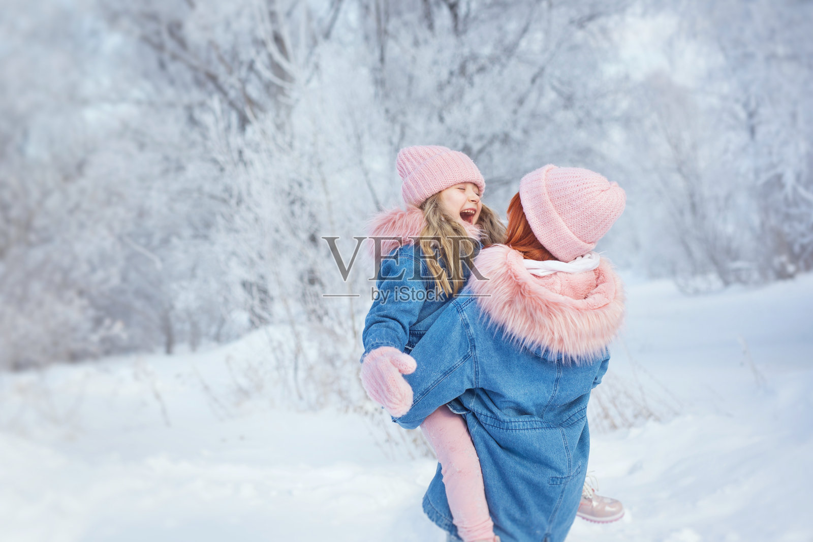 年轻的女人抱着小女孩,小女孩拥抱年轻的女人在冬天的树林里照片摄影图片