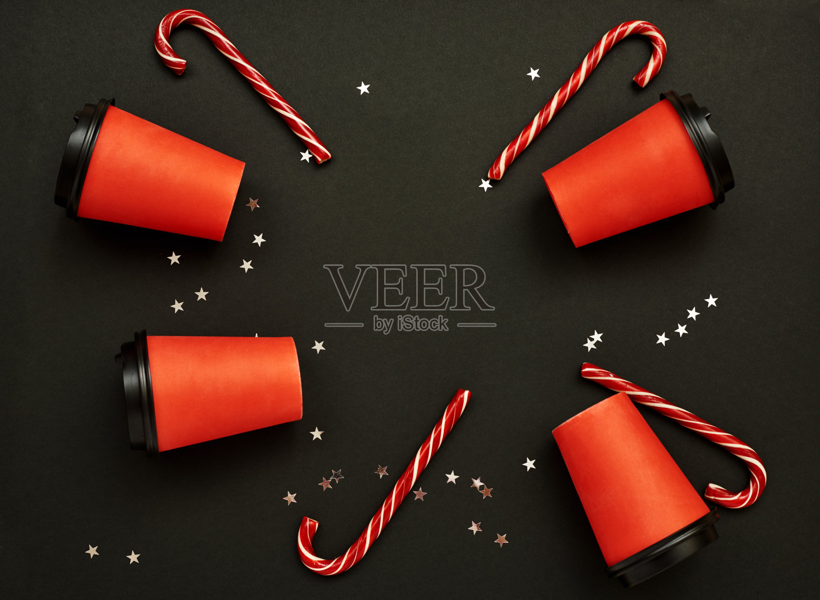 黑色背景上的甘蔗纸咖啡杯。圣诞背景与圣诞糖果手杖和星星五彩纸屑。俯视图,平铺,模型。为文本复制空间。照片摄影图片