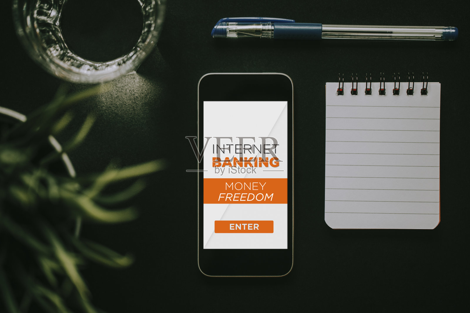 手机屏幕上有网上银行的应用程序,笔记本和笔在黑板上。照片摄影图片