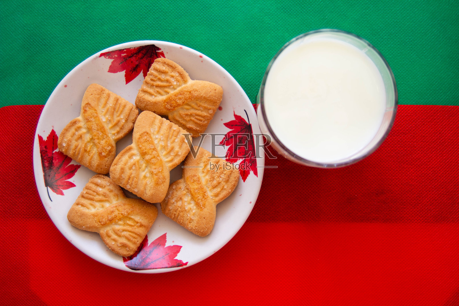 一杯牛奶和饼干或松脆饼干的盘子上有红色和绿色的背景。国家饼干日的背景。圣诞老人的圣诞早餐。美式早餐照片摄影图片