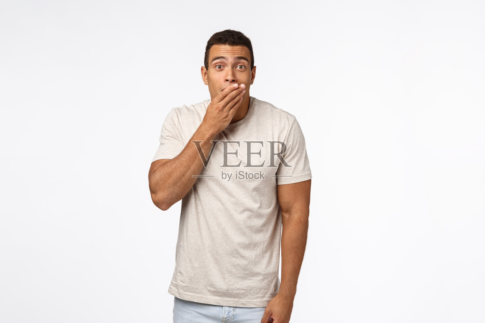 震惊的西班牙裔年轻男子穿着t恤,喘着粗气捂着嘴,目瞪口呆,说不出话来,听到难以置信的流言蜚语,目瞪口呆地站在那里,从颤抖中失去了言语照片摄影图片