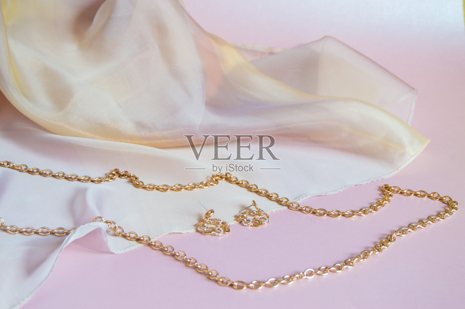 美丽珍贵的女性珠宝与钻石,特写。金项链和耳环在粉红色的丝绸背景与复制空间照片摄影图片