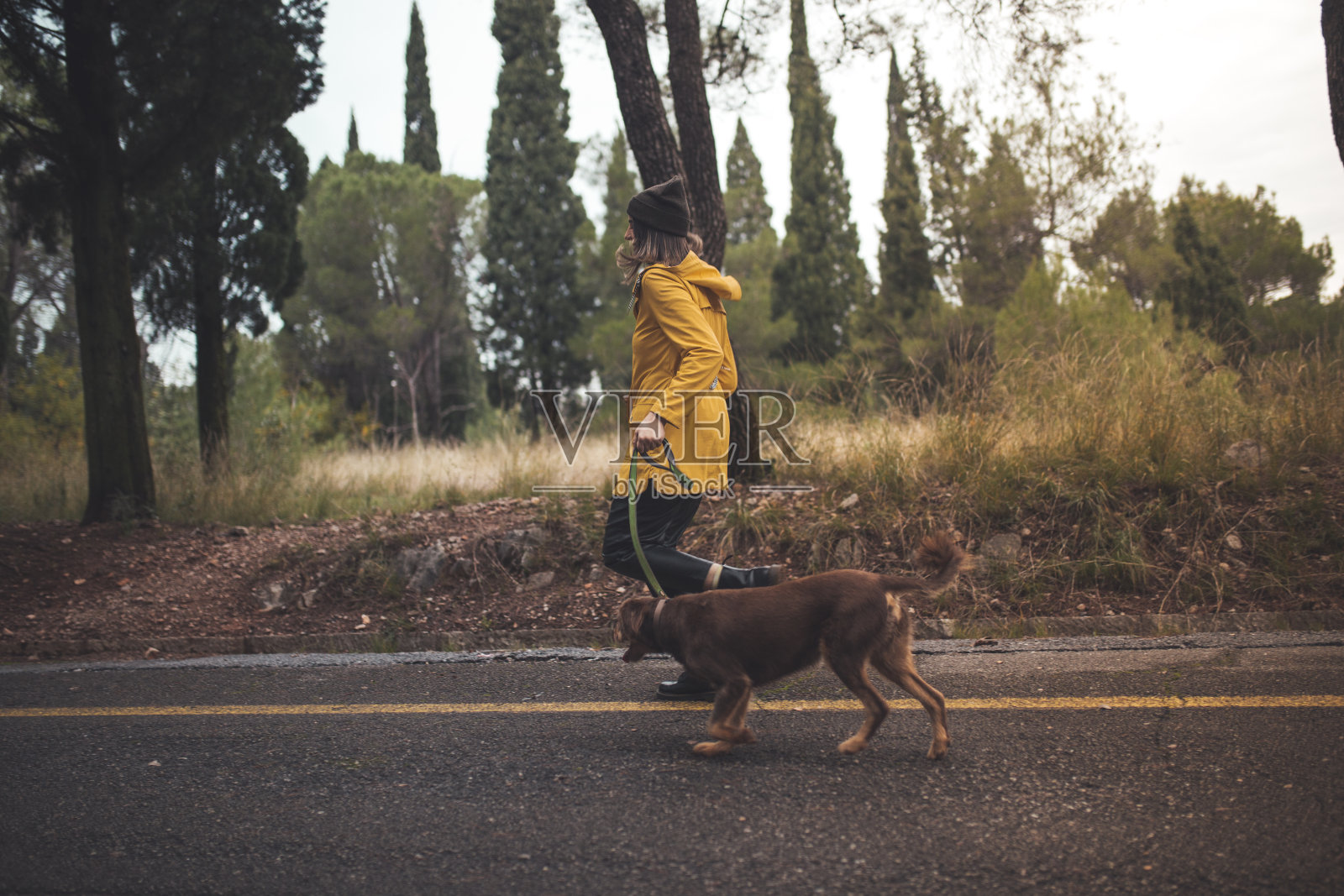穿着黄色雨衣的年轻女子和她最好的朋友哺乳动物狗在公园里跑步照片摄影图片