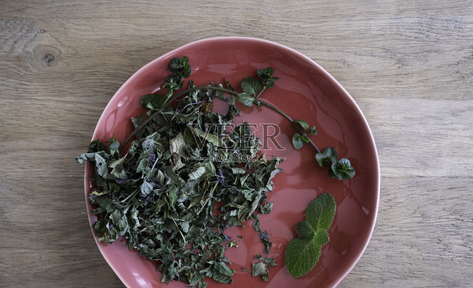 新鲜干燥的薄荷叶放在红色盘子上,木制背景,天然茶叶成分。照片摄影图片