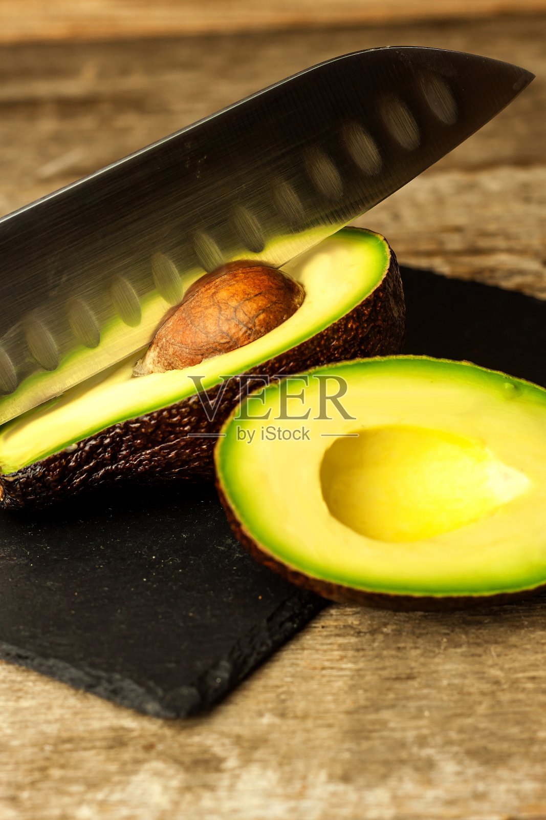 深色木材背景上的牛油果。着色。有选择性的重点。牛油果板。菜刀鳄梨片。照片摄影图片