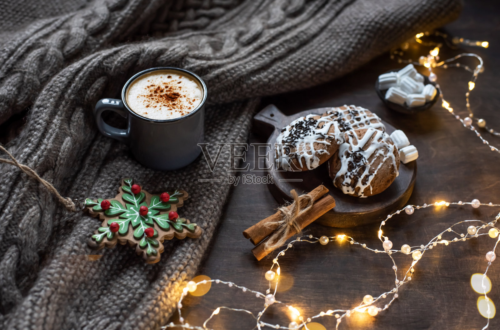 一杯加肉桂的咖啡。圣诞背景用彩灯,温暖的针织围巾。照片摄影图片