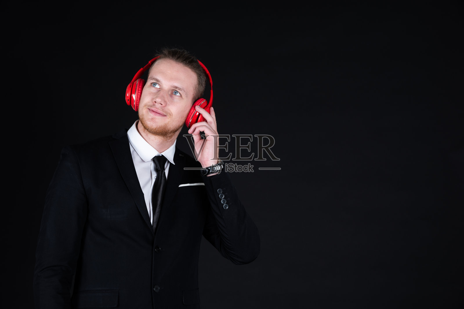 自信的商人穿着黑色西装,戴着耳机听音乐照片摄影图片