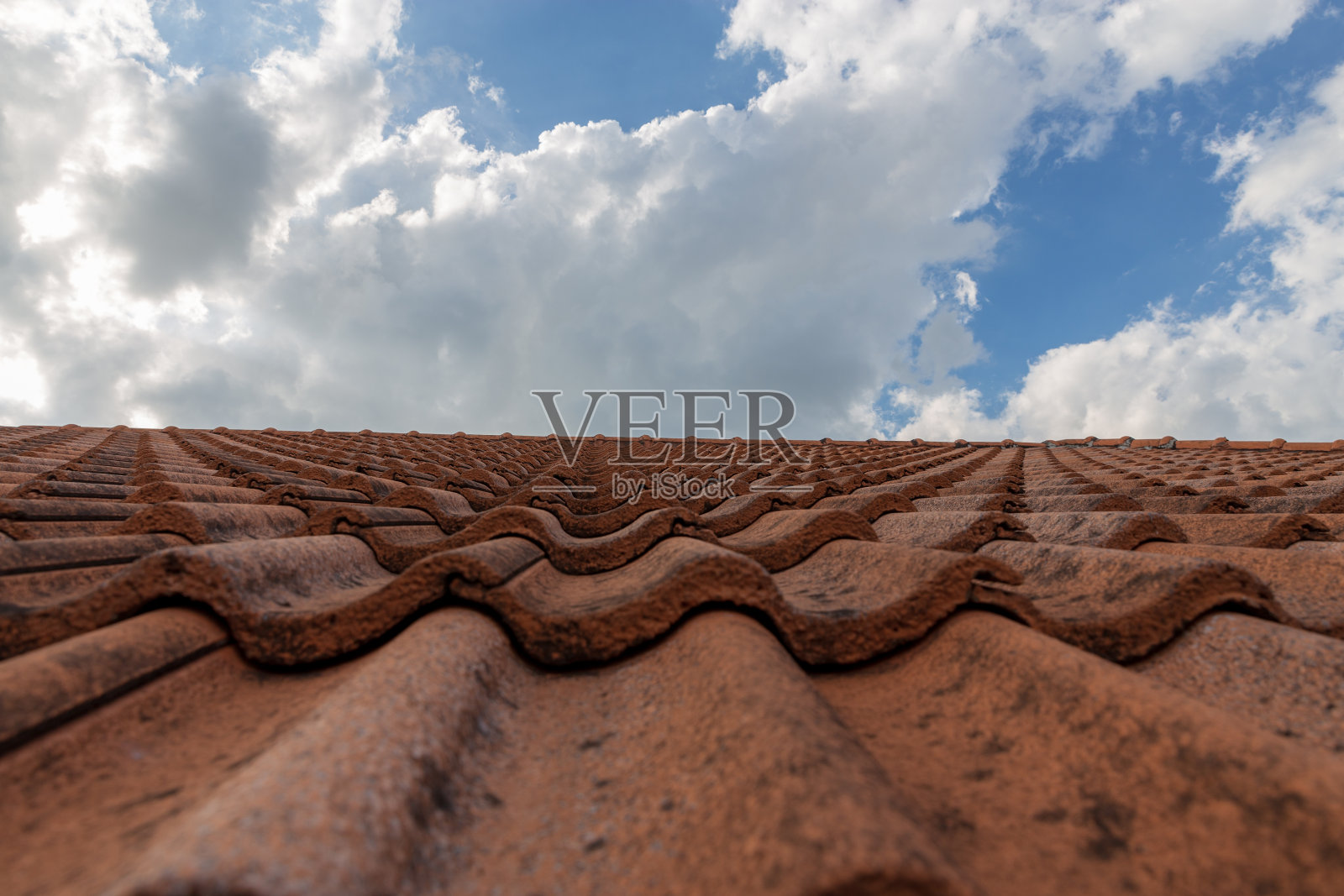 屋顶上的天空背景。棕色粘土屋顶瓦的特写。又红又旧又脏的屋顶。旧的屋顶瓦片。建筑设备盖房子。照片摄影图片