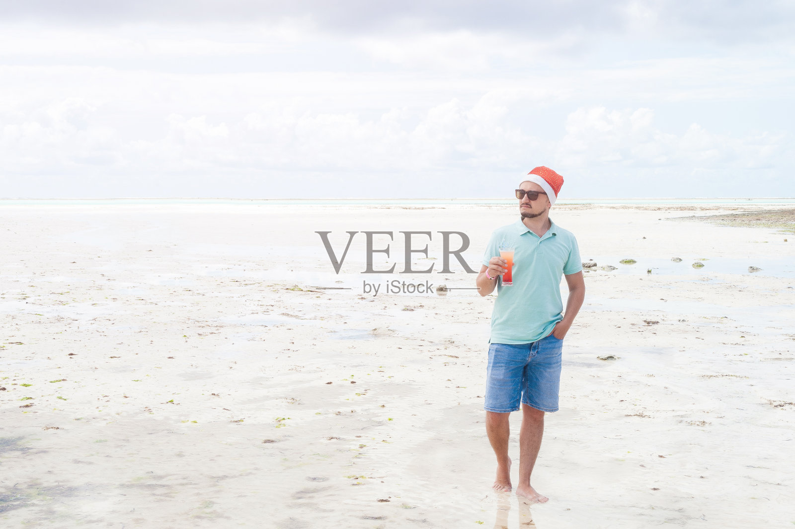 一个留着胡子戴着圣诞帽的男人在桑给巴尔岛的海滩上喝着鸡尾酒照片摄影图片