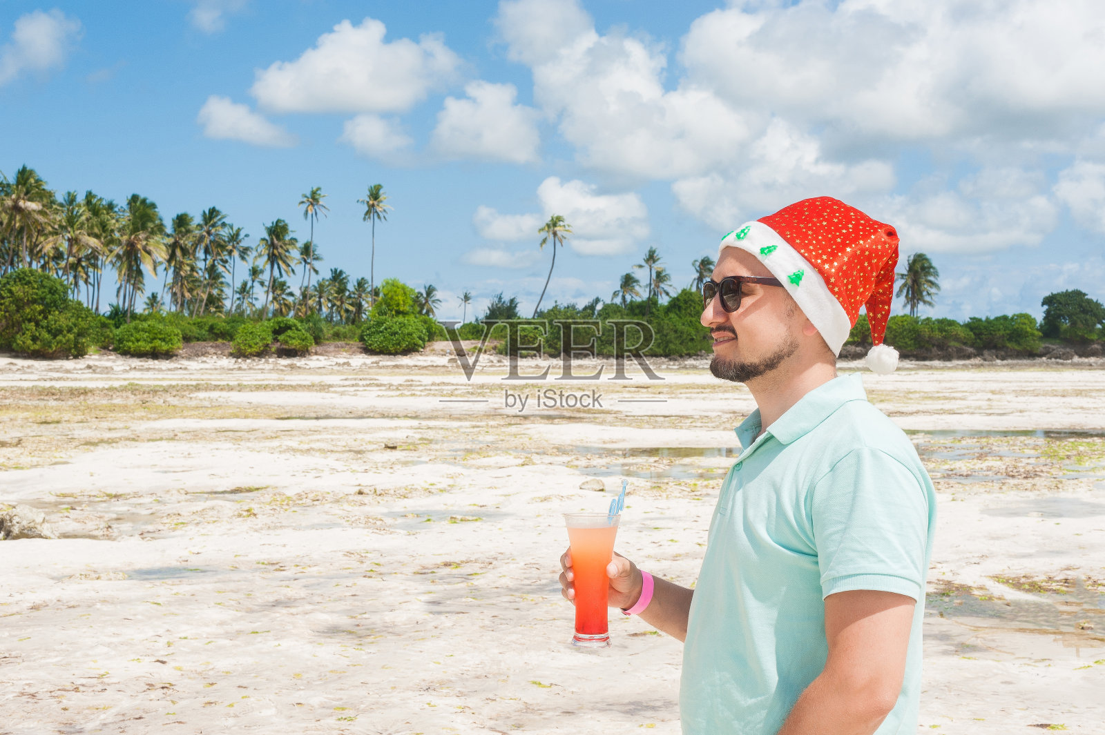 一个留着胡子戴着圣诞帽的男人在桑给巴尔岛的海滩上喝着鸡尾酒照片摄影图片