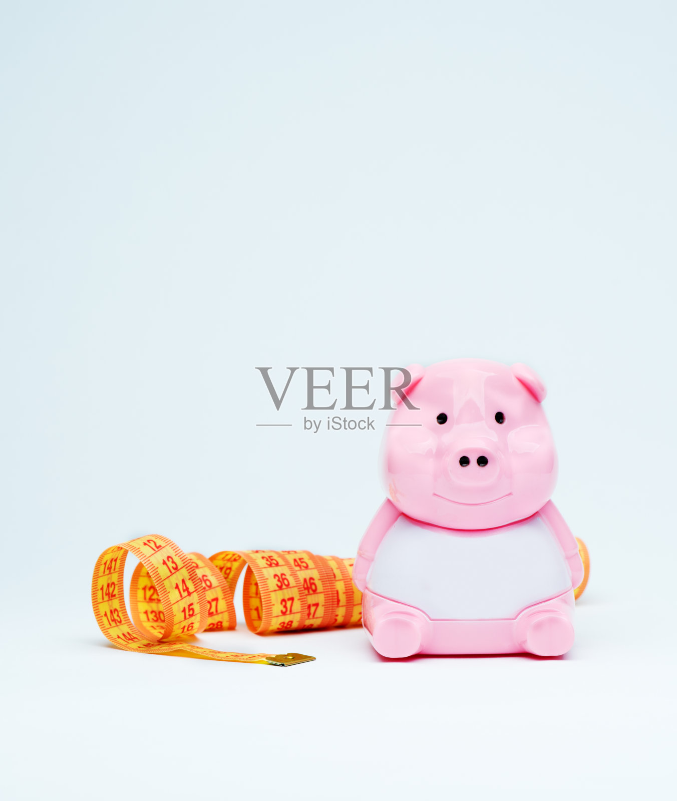 蓝色背景上带软尺的存钱罐:营养学、投资与健康概念照片摄影图片