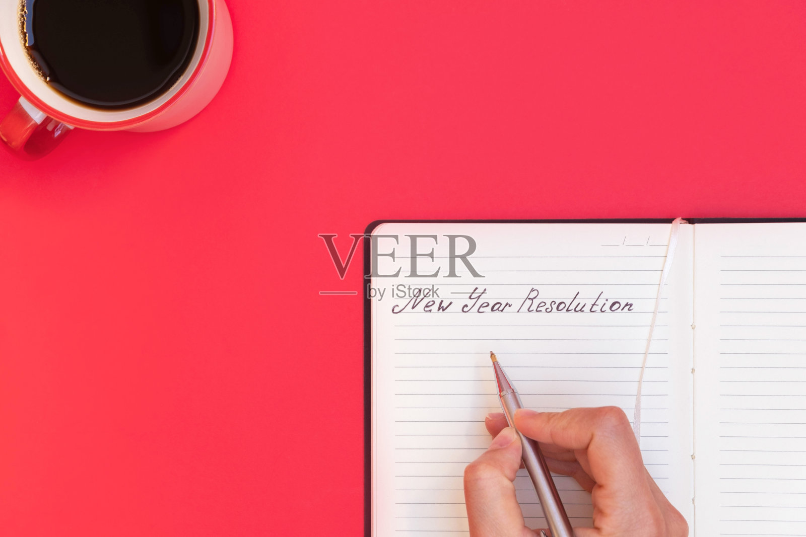 俯视:女性手持笔在笔记本上书写新年计划,红背景上有咖啡杯,留白区域照片摄影图片
