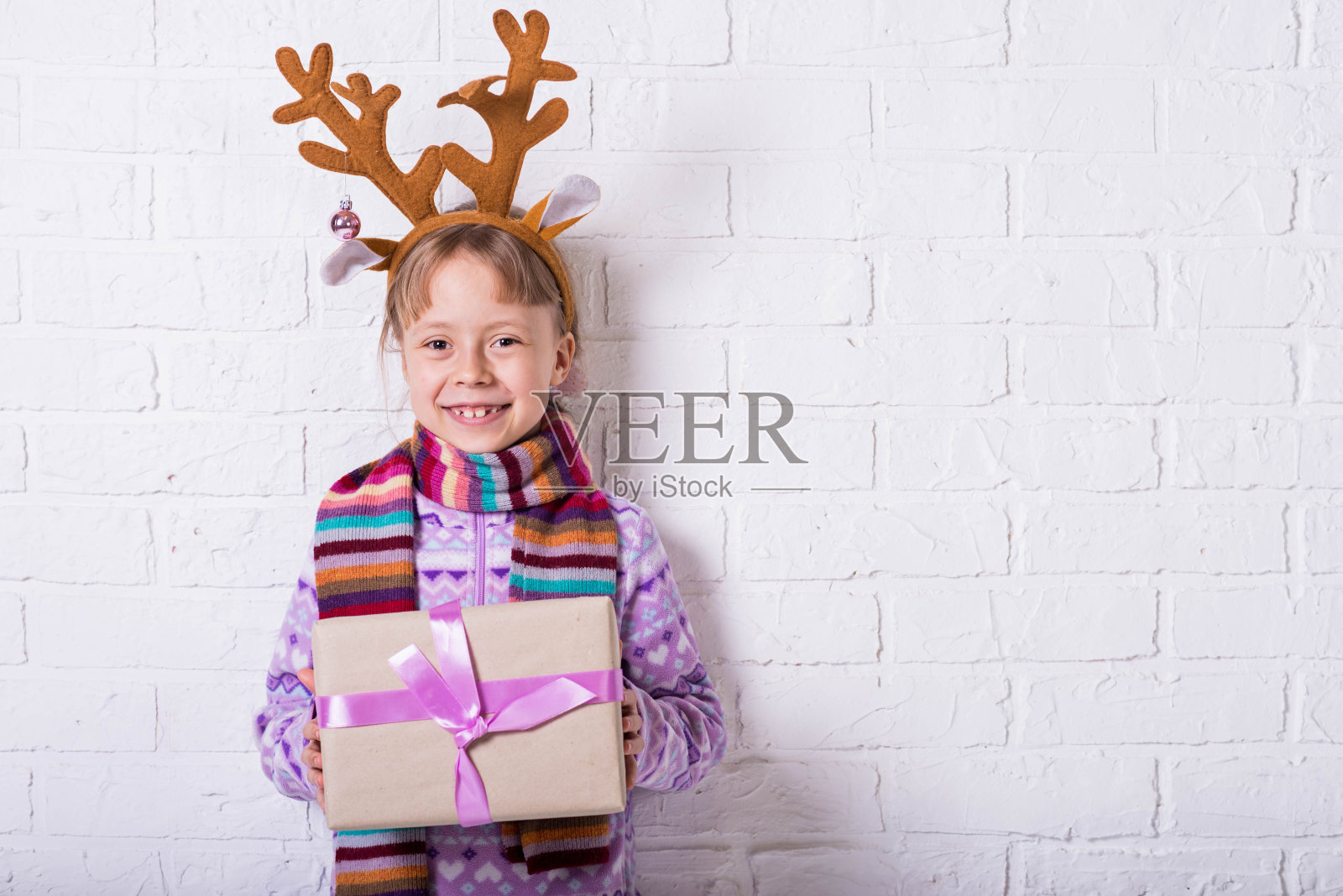 可爱的小女孩戴着鹿角,手里拿着圣诞礼物,圣诞背景。照片摄影图片