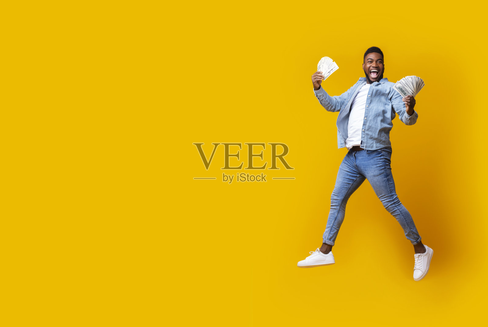 快乐的黑人男子拿着钱,在空中跳跃并兴奋地尖叫照片摄影图片