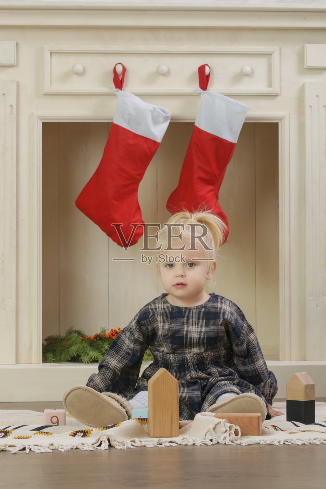 可爱的蹒跚学步的小女孩在室内用红色的圣诞袜子装饰的木制壁炉前玩耍,在家里过寒假照片摄影图片