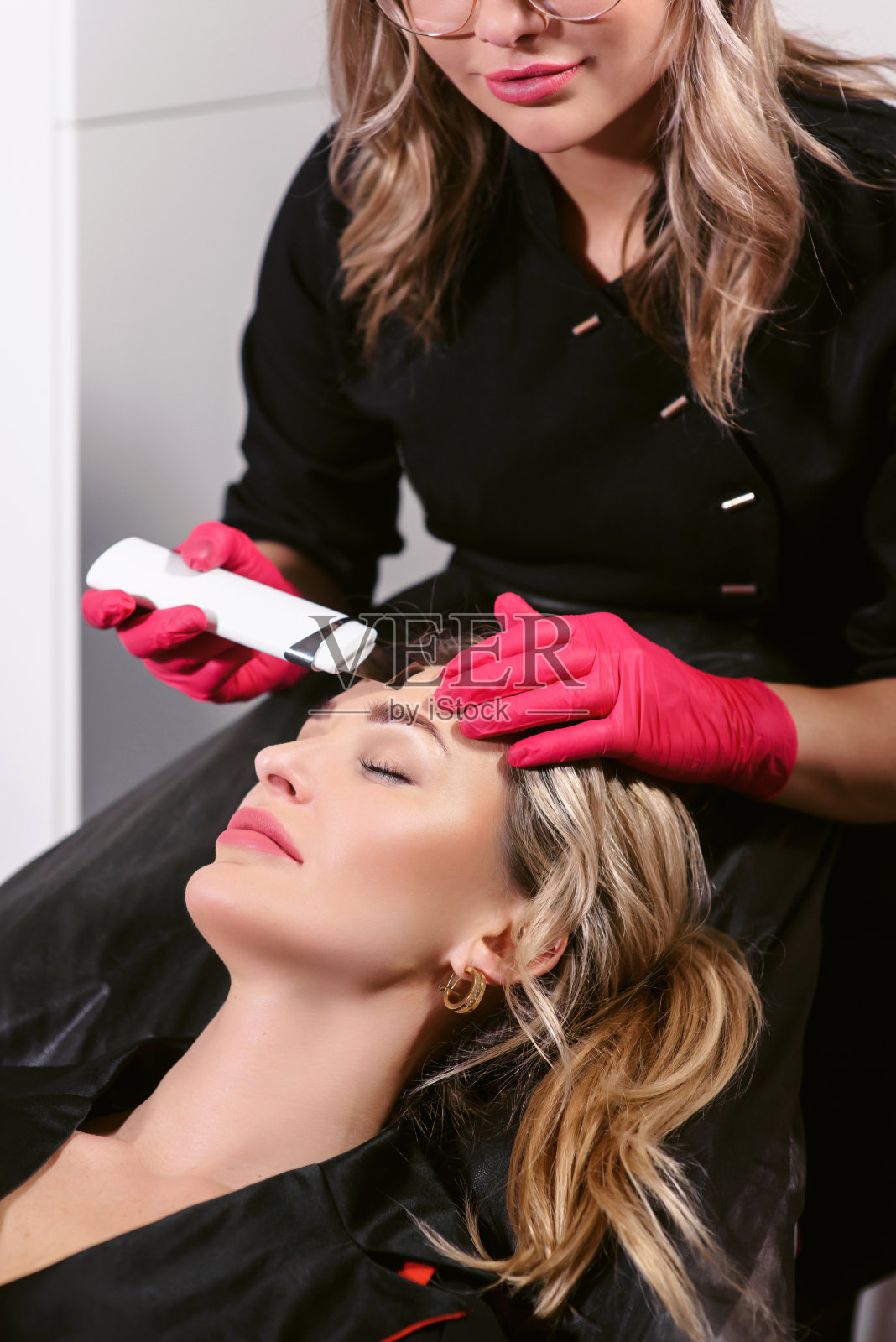 美容师在起作用。近距离女人接受脸部超声波脱皮在现代美容沙龙。在美容诊所接受射频提容的女性病人。照片摄影图片