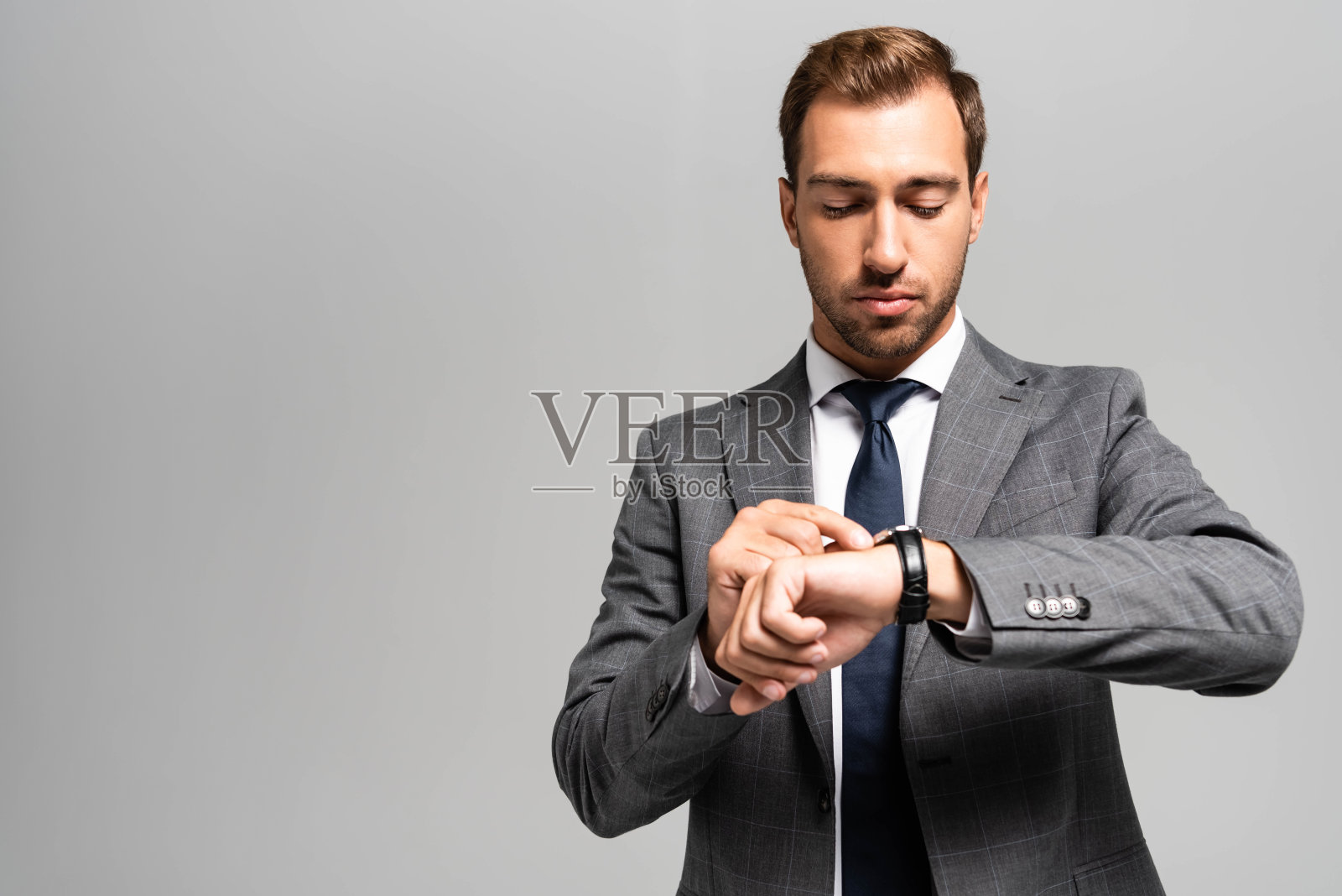 英俊的商人西装看着手表孤立在灰色照片摄影图片
