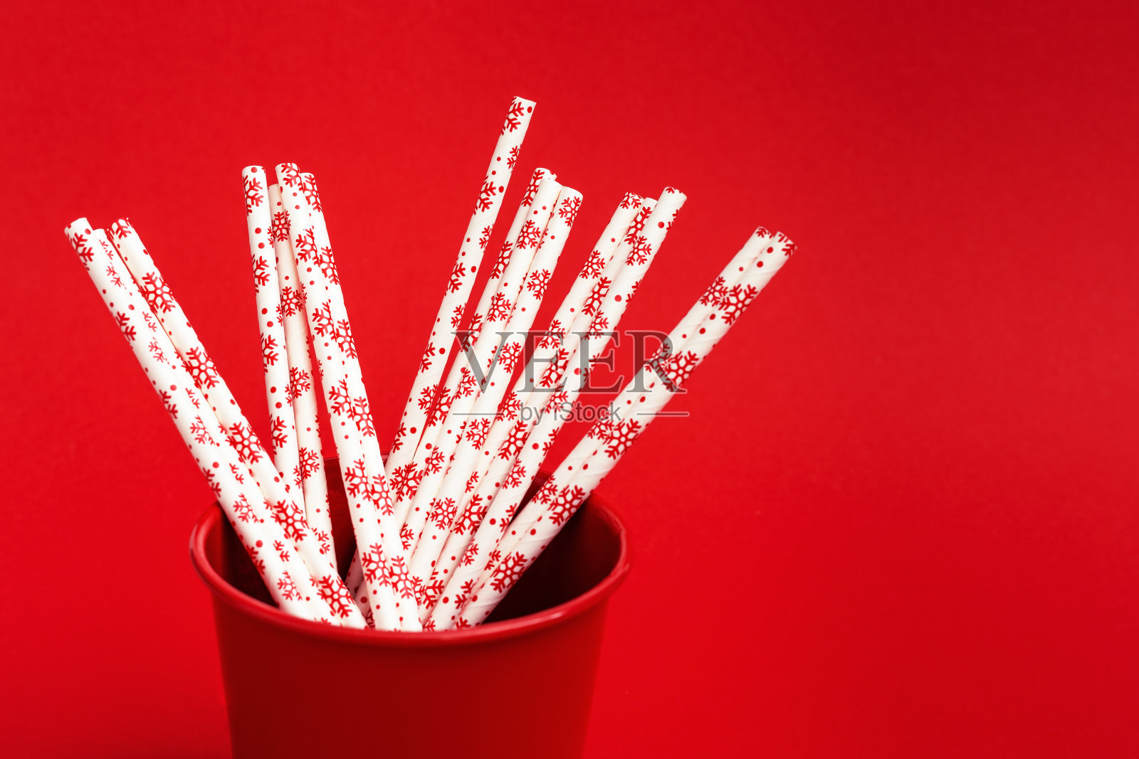 明亮的纸饮吸管与冬季图案在金属桶在红色表面与拷贝空间。新年或圣诞节的庆祝背景。照片摄影图片