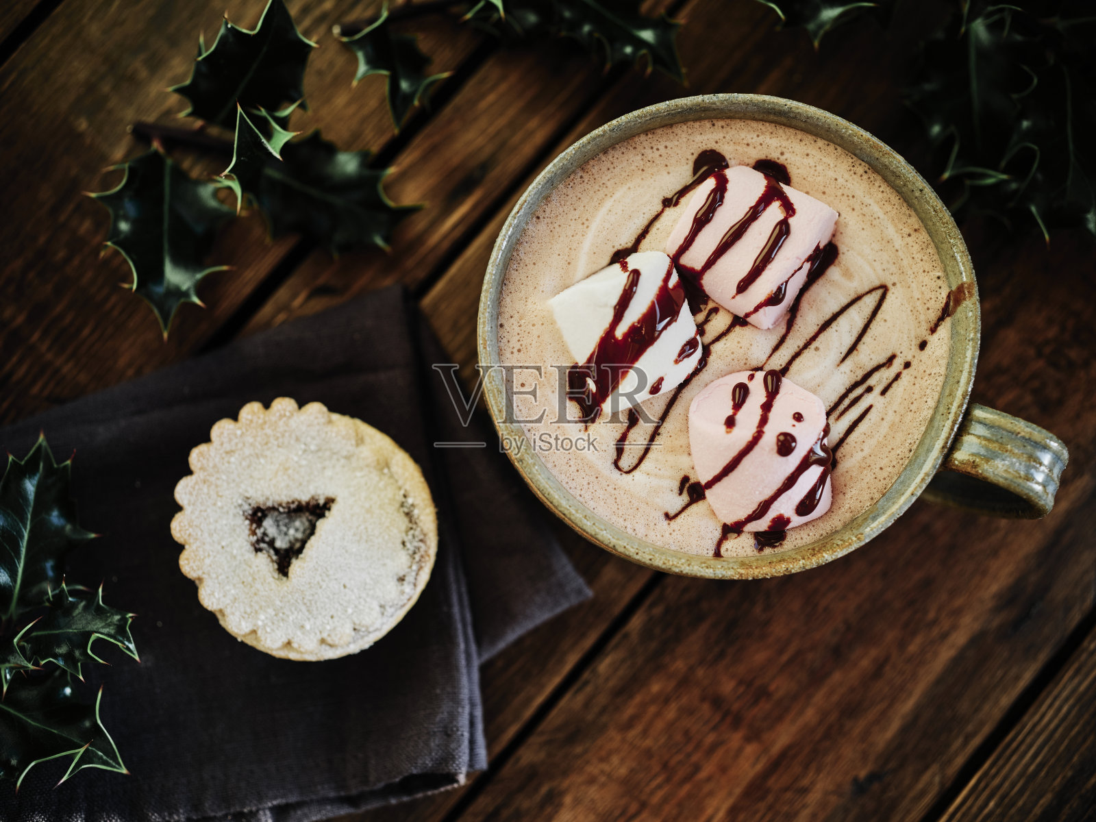 奶油热巧克力配上3块棉花糖和巧克力酱,放在一个黑色的乡村木质桌面上,配上肉馅派和节日冬青树。照片摄影图片