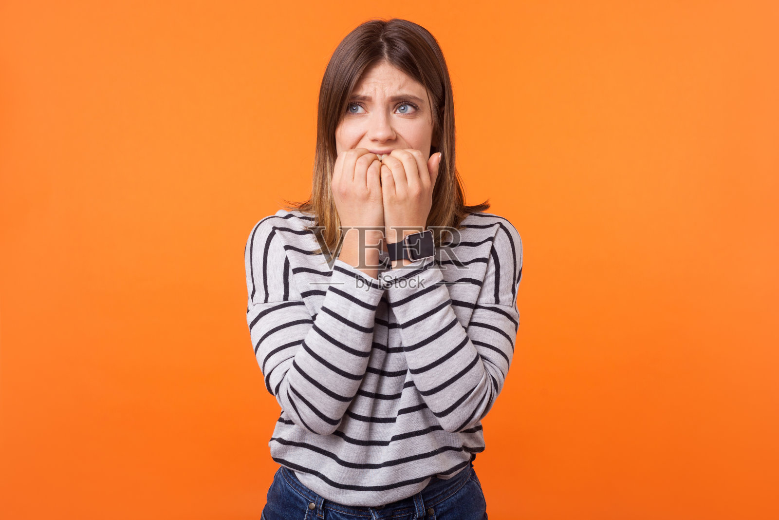 紧张抑郁的年轻女子肖像,棕色头发,长袖条纹衬衫,室内工作室拍摄,橙色背景照片摄影图片