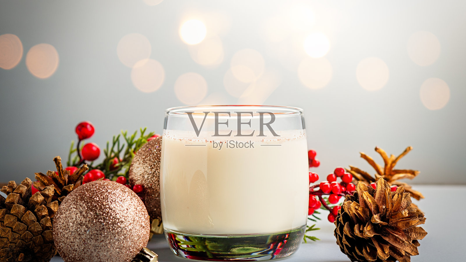 传统的圣诞鸡尾酒蛋奶酒与鸡蛋,酒精,磨碎的肉豆蔻和肉桂特写。传统的甜饮料在木桌上,红色的装饰和松果照片摄影图片