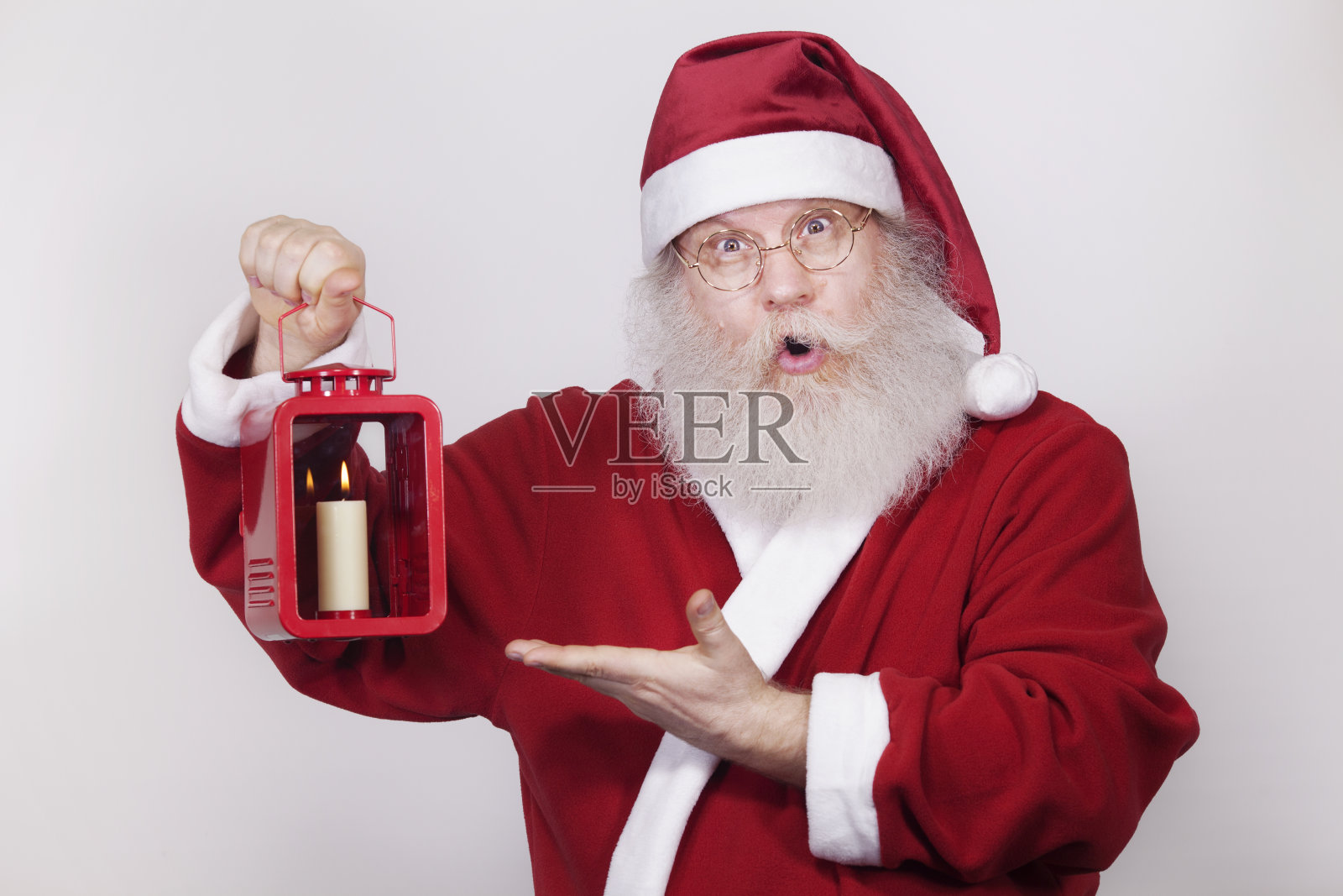 圣诞老人用点燃的蜡烛指着一盏灯。照片摄影图片