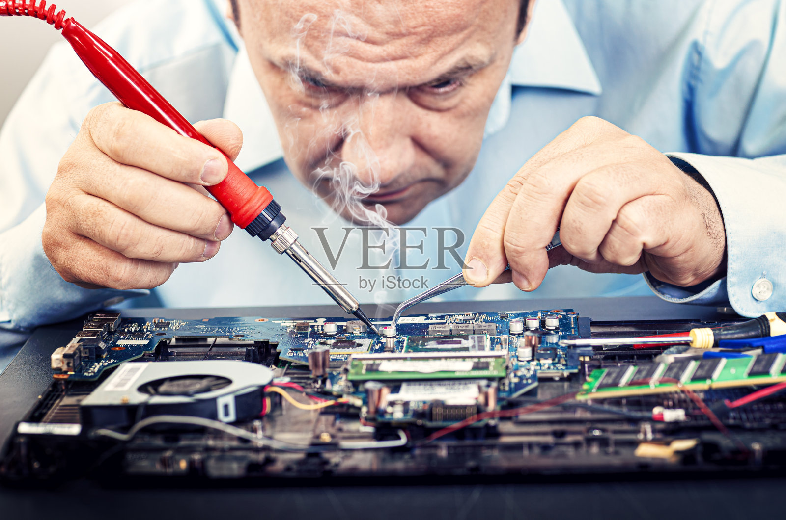 一位电子工程师正在修理一台笔记本电脑。工程师正在焊接计算机。照片摄影图片