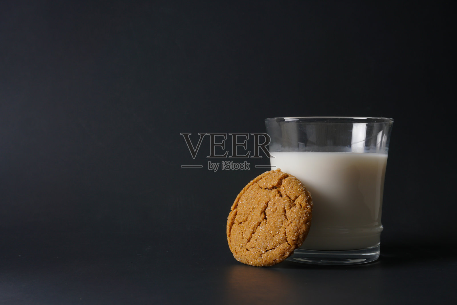 一块姜糖蜜饼干靠在一杯冷牛奶上,背景是黑色的,有拷贝空间照片摄影图片