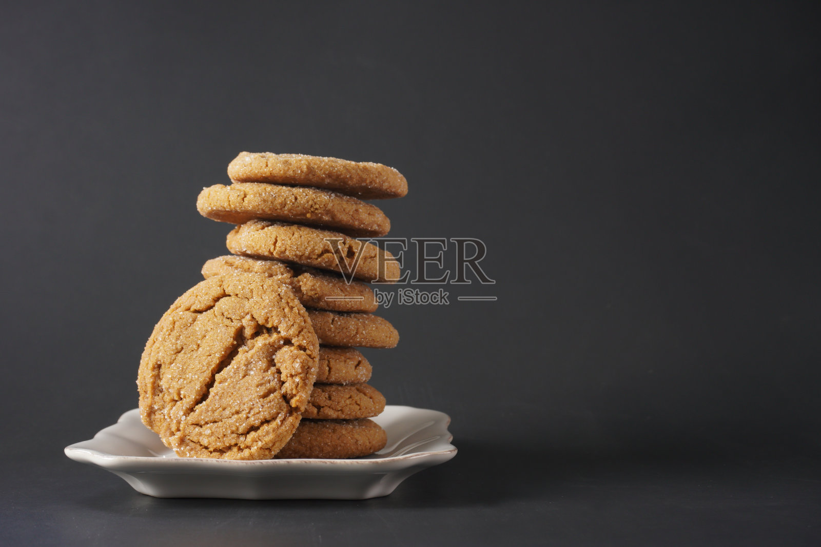 一块脆脆的姜饼斜靠在一堆饼干上,放在一个白色的黑色背景的盘子里照片摄影图片