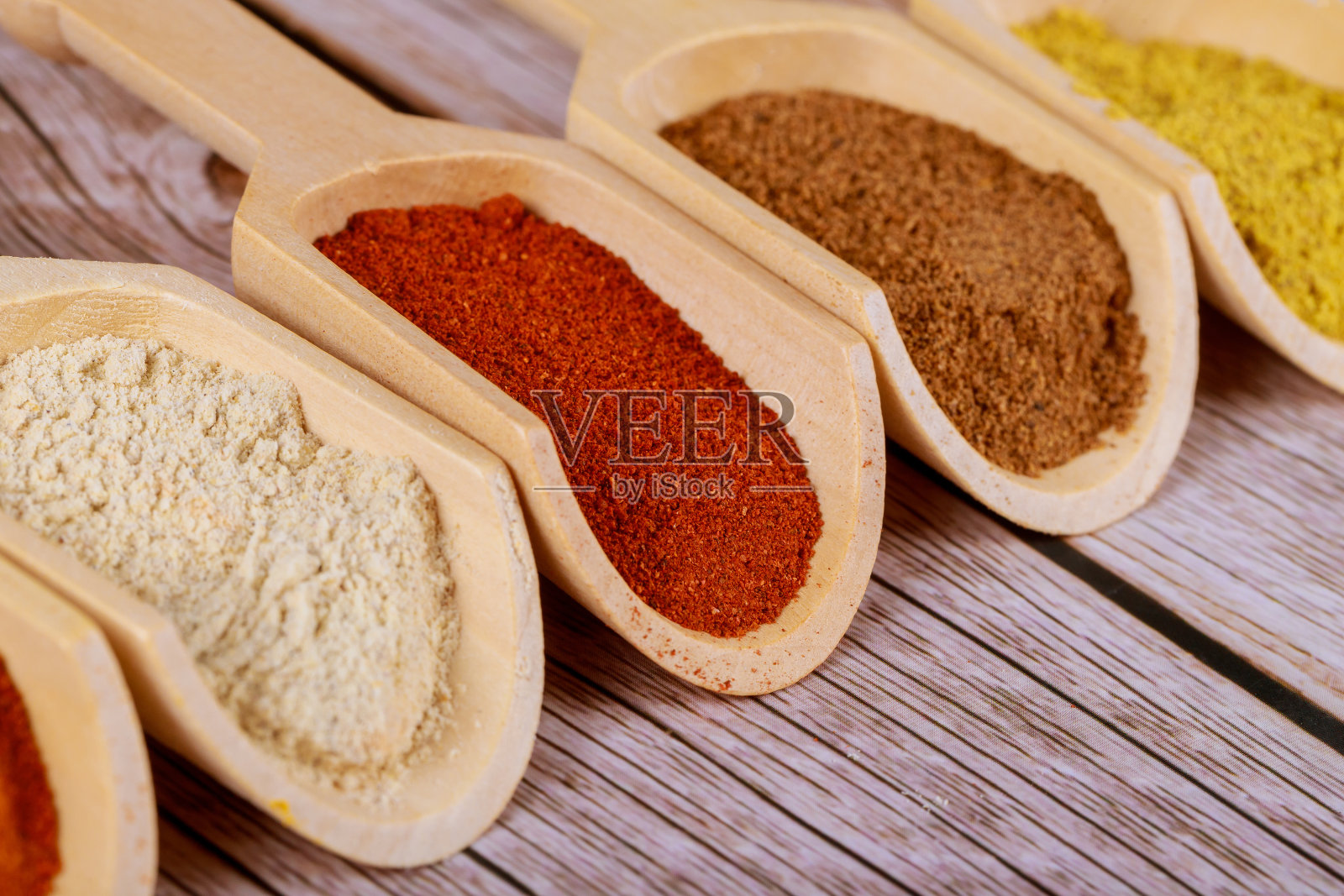 芥末粉,辣椒粉,咖喱和大蒜用木勺放在木质背景上。照片摄影图片