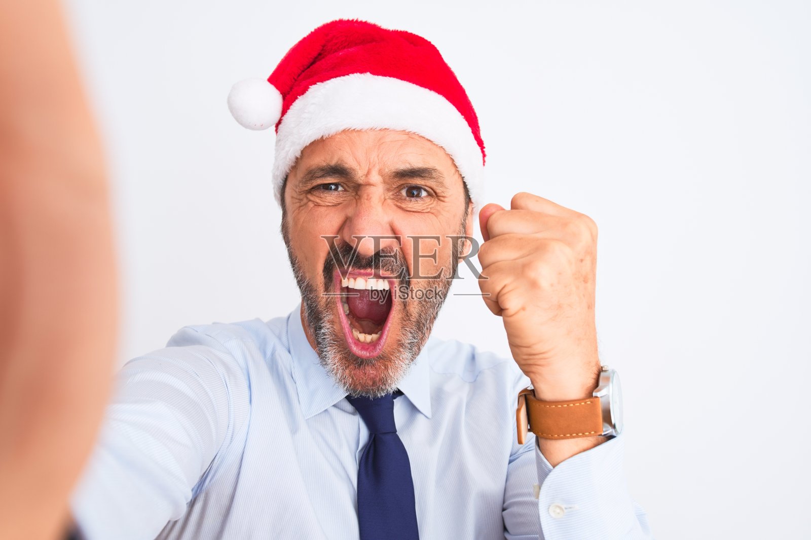 中年商人戴着圣诞帽在孤立的白色背景下自拍生气和沮丧的大喊与愤怒,疯狂和大喊与举手,愤怒的概念照片摄影图片