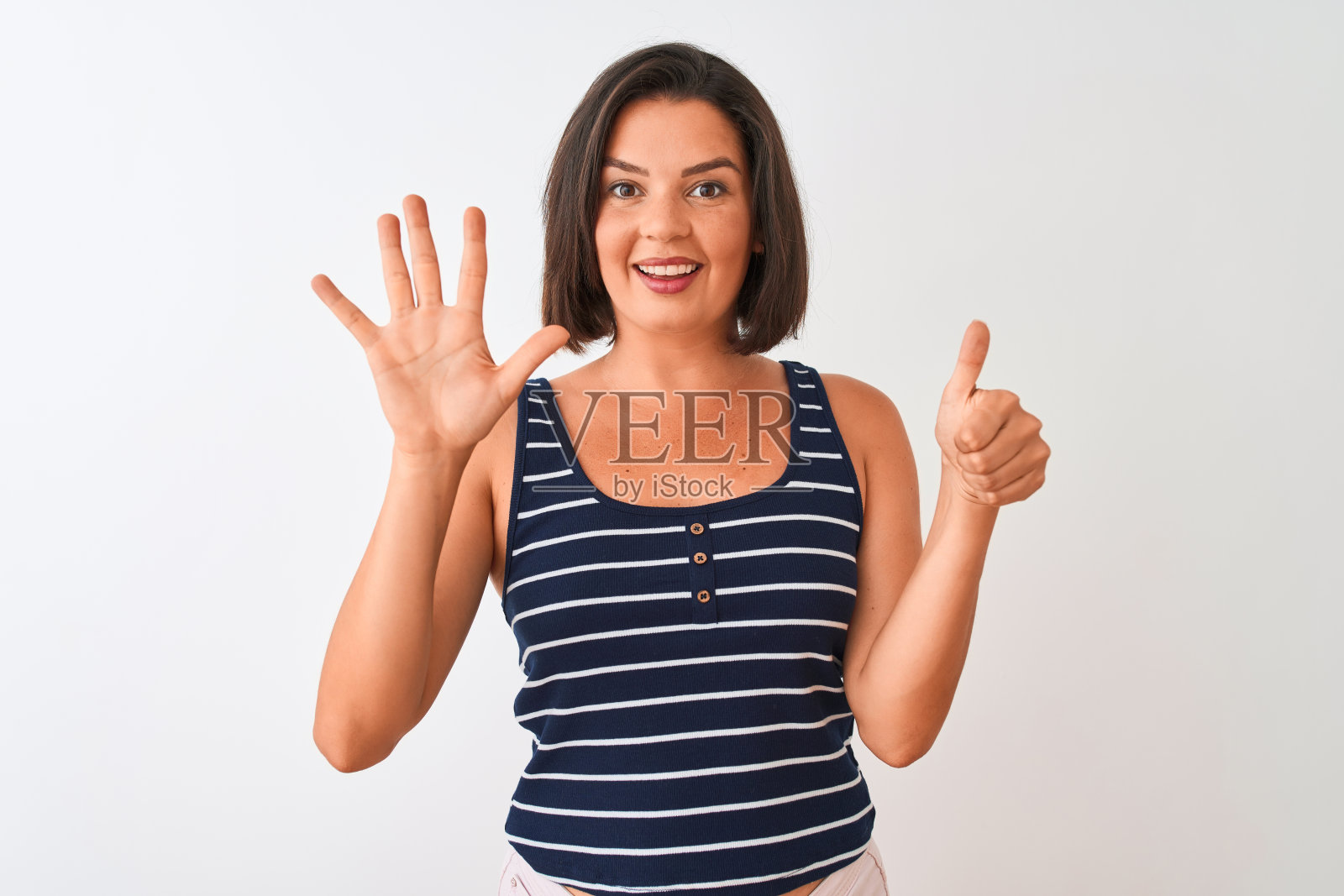 年轻美丽的女人穿着蓝色条纹t恤站在孤立的白色背景显示和指向6号手指,同时自信和快乐的微笑。照片摄影图片