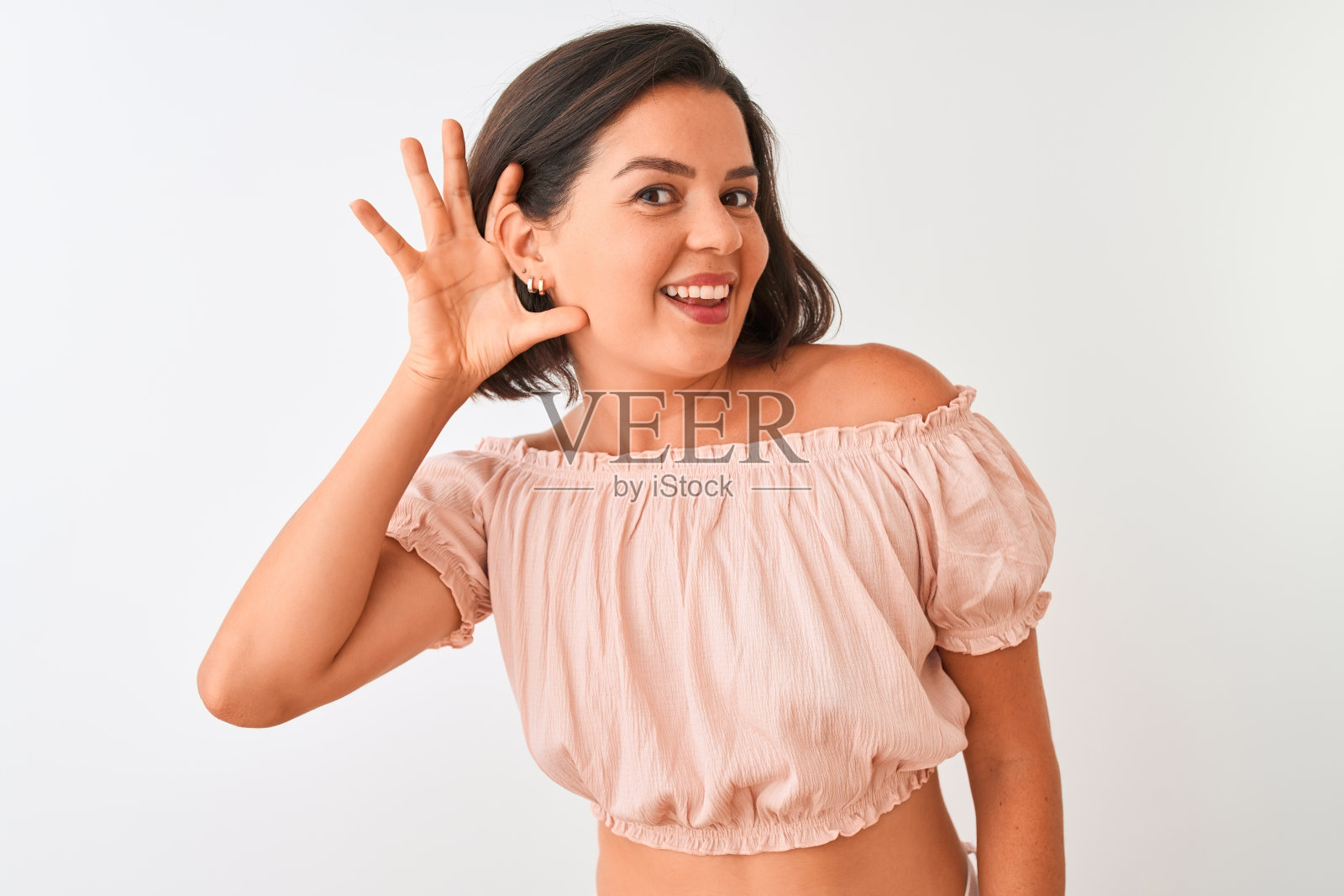 年轻美丽的女人穿着休闲t恤站在孤立的白色背景微笑与手捂耳朵听谣言或八卦。耳聋的概念。照片摄影图片