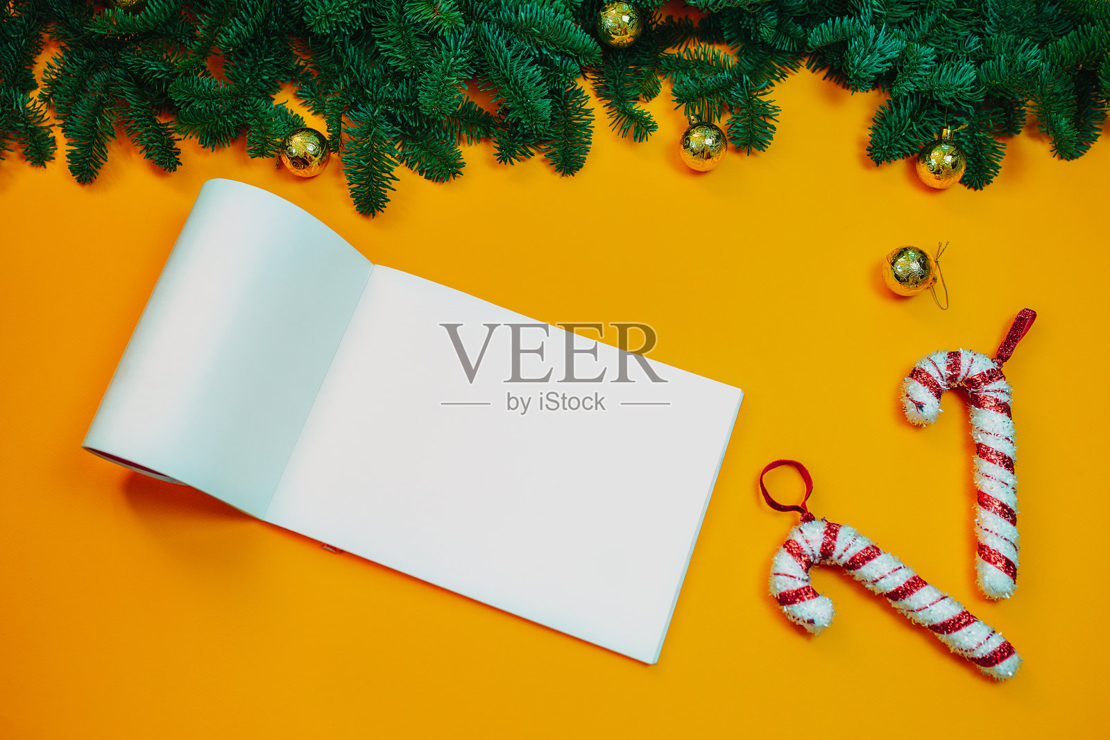 在橙色的背景上,用天然冷杉树枝平铺着圣诞装饰品和糖果手杖。有拷贝空间的圣诞卡。给圣诞老人的信用冷杉树枝环绕。照片摄影图片