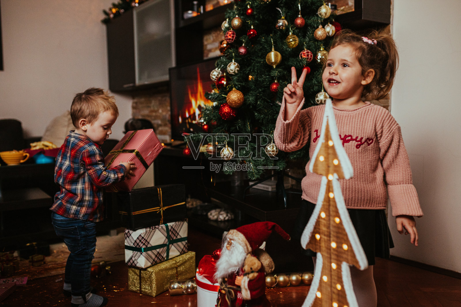 蹒跚学步的弟弟和妹妹在家里打开圣诞礼物照片摄影图片