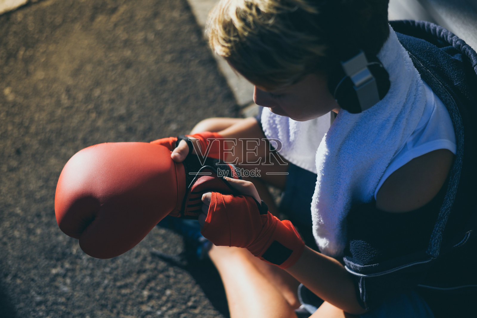 英俊的年轻男子手里拿着拳击带,看着手套坐在路上。男孩一边听着音乐,一边准备进行拳击训练。运动,青春,自由时间,决心和竞争观念照片摄影图片