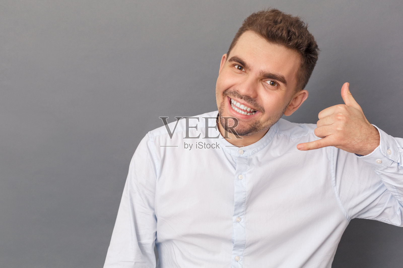 自由泳。青年站在孤立的灰色演播室显示呼叫手势微笑愉快的特写照片摄影图片