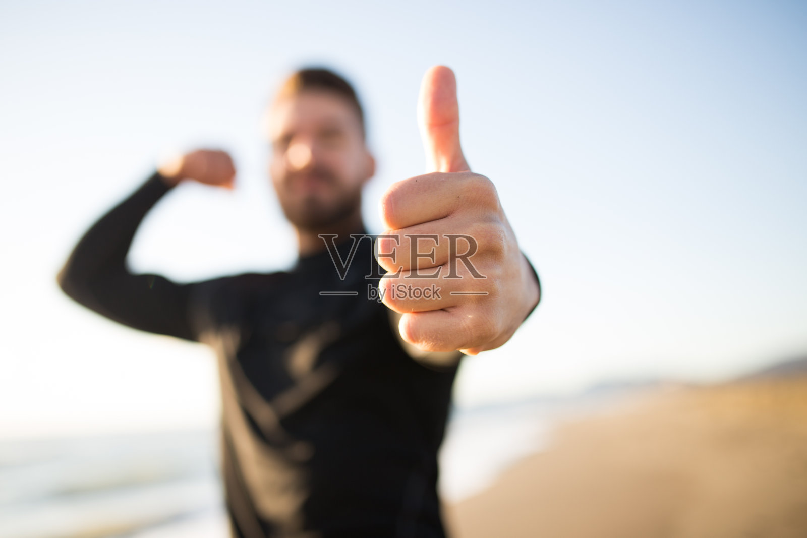 一个年轻的跑步运动员在海滩上竖起大拇指的照片。照片摄影图片