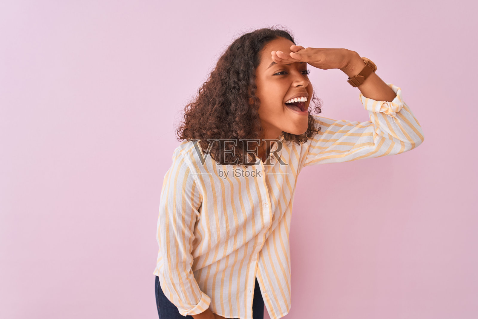 年轻的巴西女人穿着条纹衬衫站在孤立的粉红色背景非常幸福和微笑看远与手在头上。搜索概念。照片摄影图片