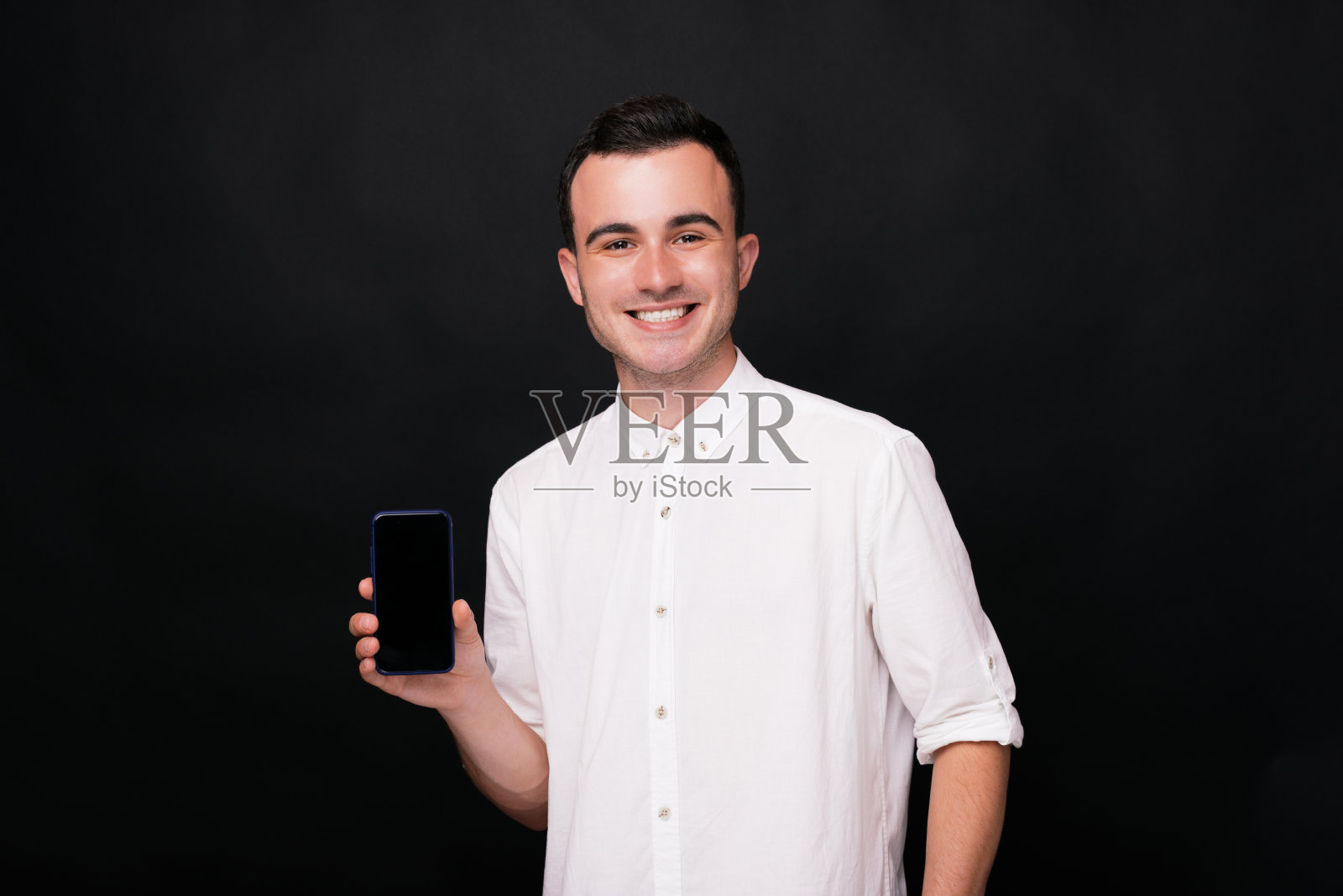 一个年轻人在黑色背景上展示他的手机空白屏幕上的广告。照片摄影图片