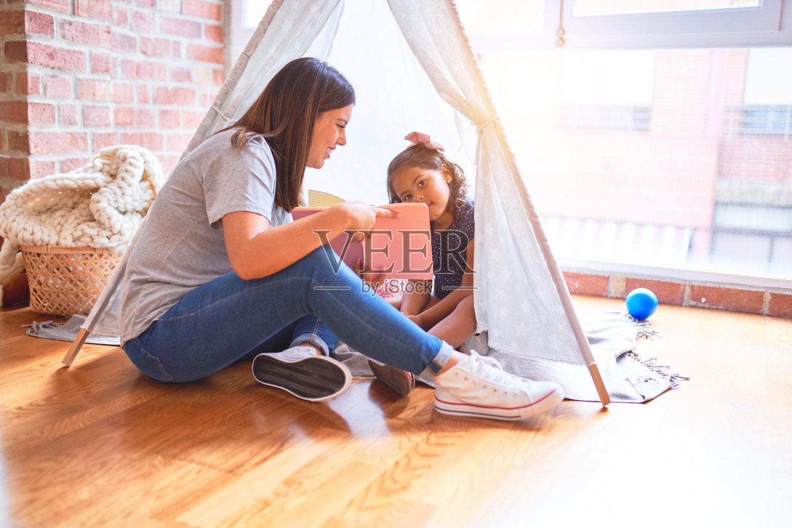 在幼儿园里,漂亮的老师正给坐在地板上的小女孩读书照片摄影图片