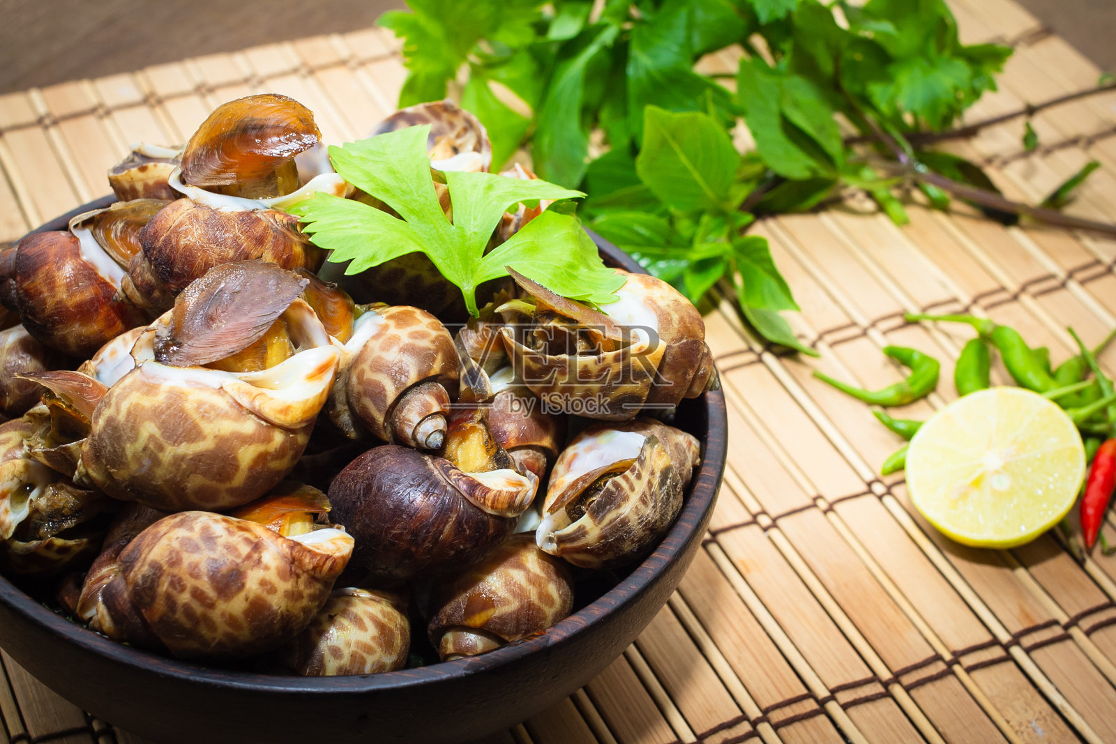用木碗煮熟的巴比伦莲或贝类,桌上放柠檬和辣椒。海鲜照片摄影图片