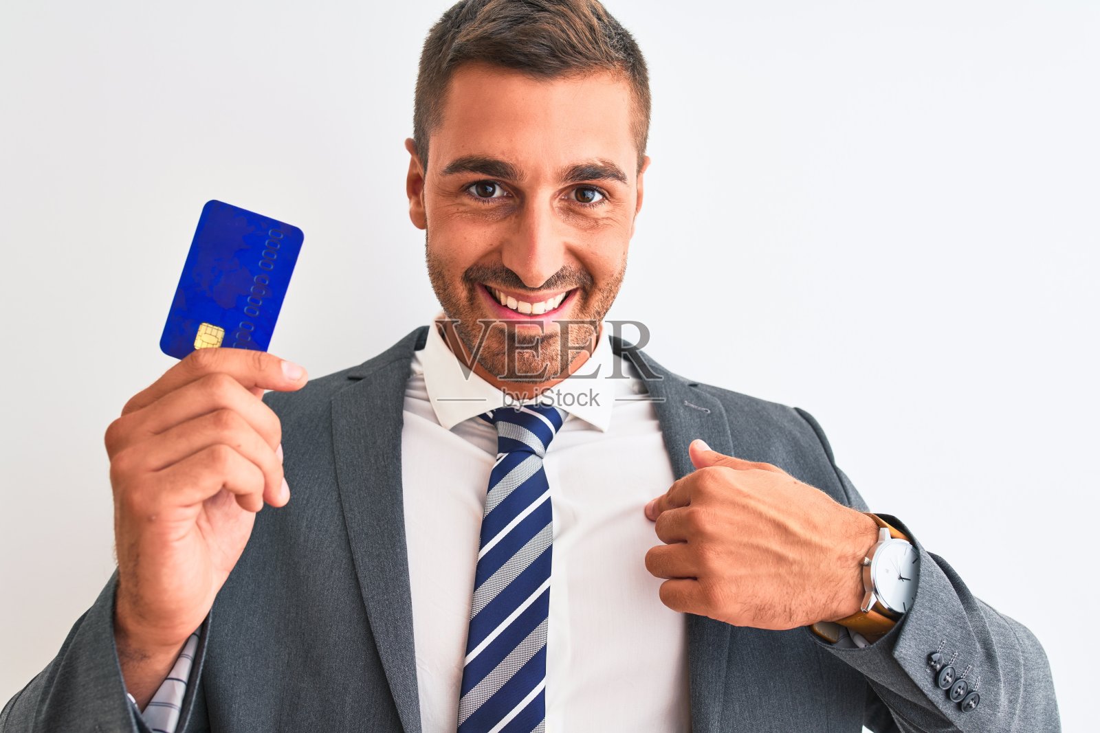 年轻英俊的商人拿着信用卡在孤立的背景与惊讶的脸指向自己照片摄影图片