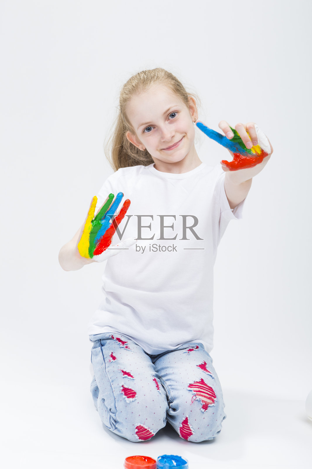 孩子的概念。微笑的年轻女孩的肖像显示凌乱多彩的手鲜艳的油漆工艺。在白色的背景下。垂直的形象定位照片摄影图片