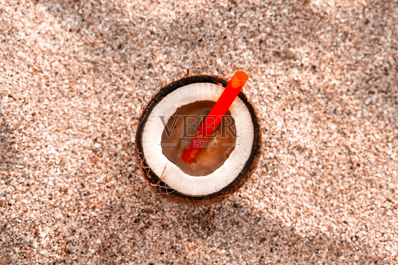 上面的椰子鸡尾酒在海滩上的观点。红色的椰子草在沙滩上,映衬着蓝天和大海。复制空间,户外活动。照片摄影图片