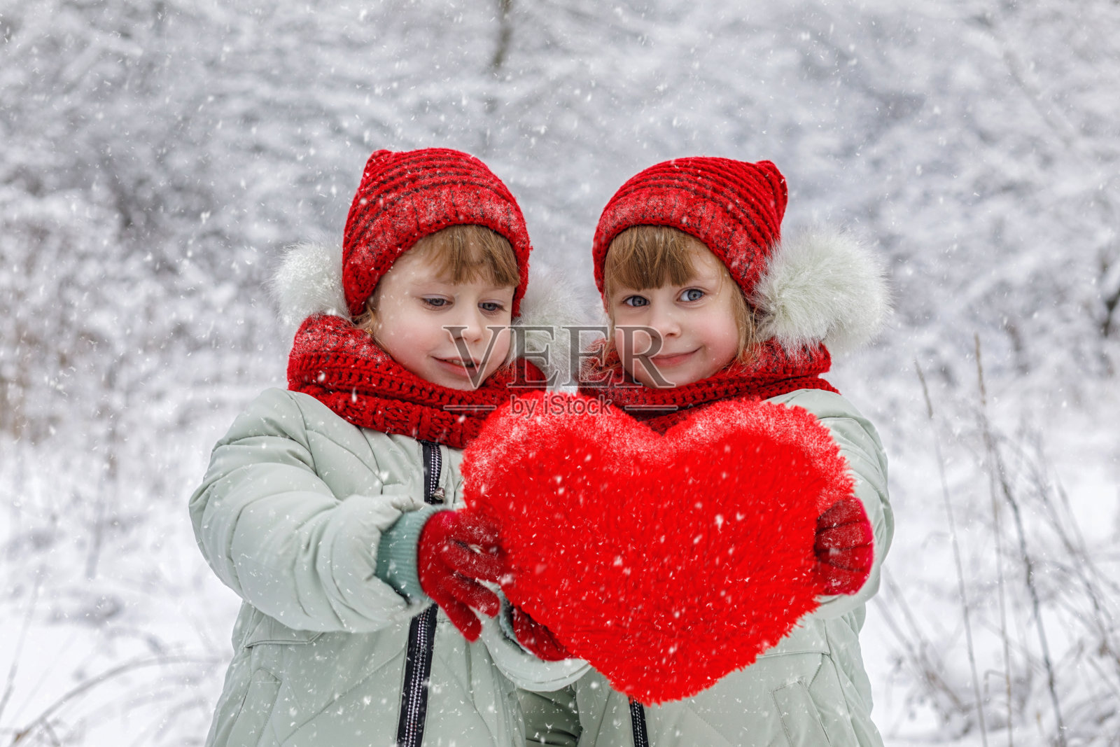 两个双胞胎小女孩在他们的手中展示了一个巨大的毛绒红色的心。照片摄影图片