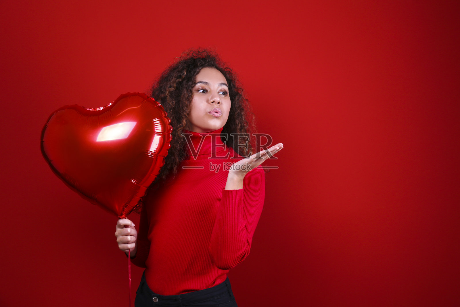 漂亮的年轻女子举着氦气气球在红墙上方摆姿势。照片摄影图片