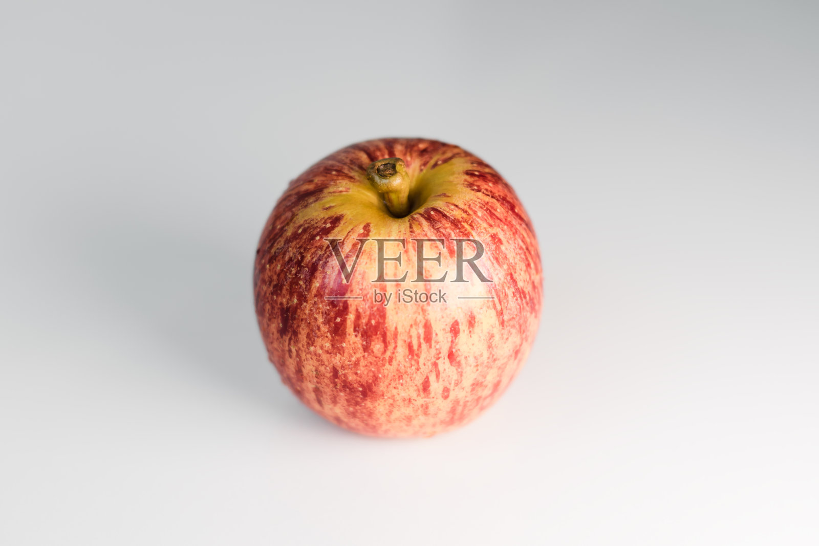 新鲜的红黄相间的苹果和水滴放在白色光滑的餐桌上。照片摄影图片