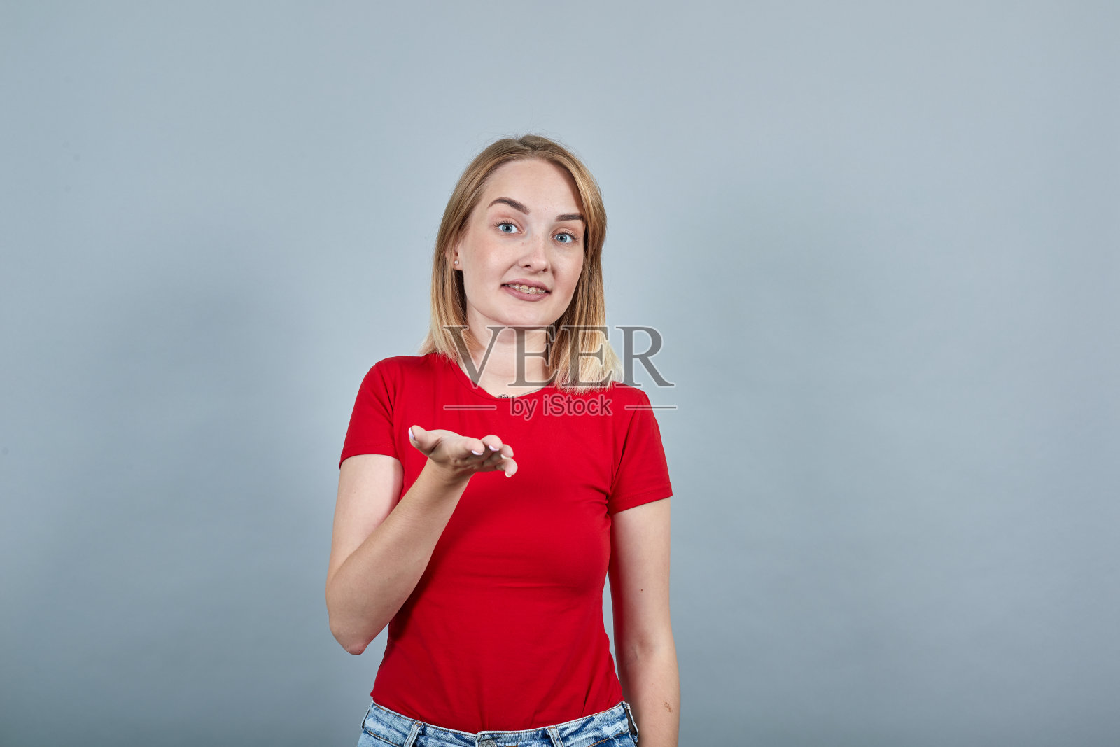 穿着红衬衫的年轻女子站在那里,看着镜头,用手指着镜头照片摄影图片